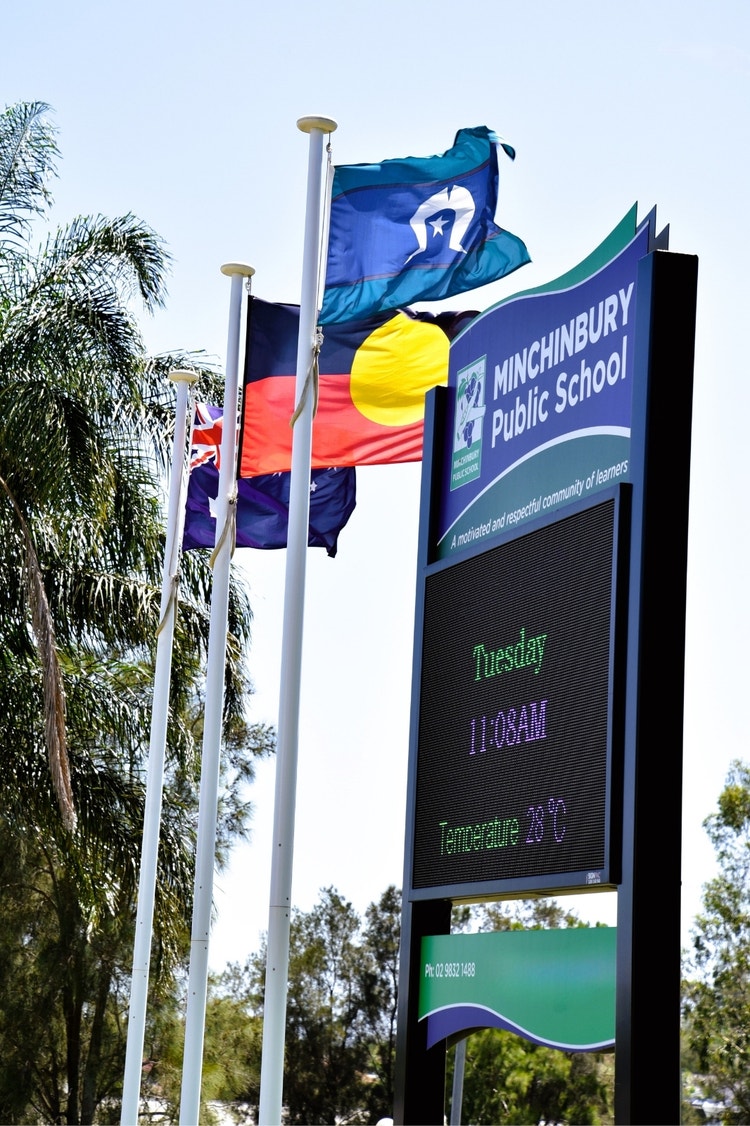 The school sign at the front fence, with the Australian, Aboriginal and Torres Strait flags in the midground.